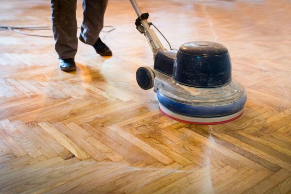 Close-up of a floor sander being used on wooden parquet flooring.